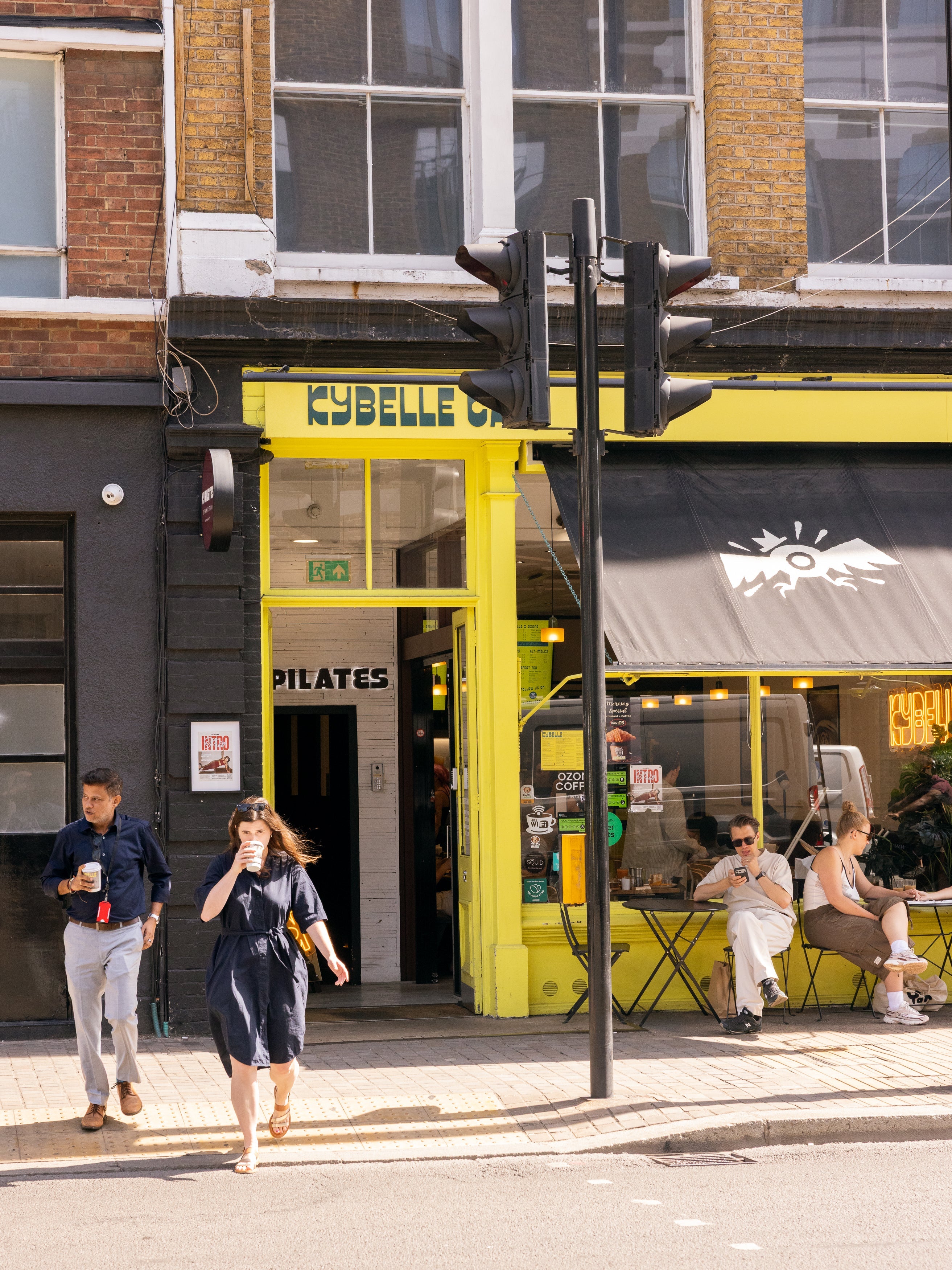 Yellow Kybelle Café shopfront on the corner near Old Street station, Shoreditch, with customers walking by with coffee